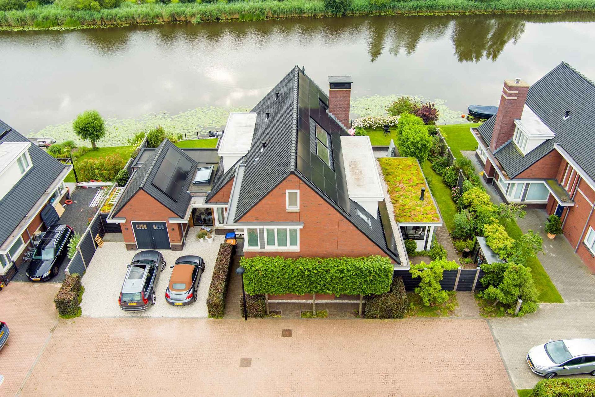 Een luchtfoto van een huis met een groen dak en auto's die ervoor geparkeerd staan.