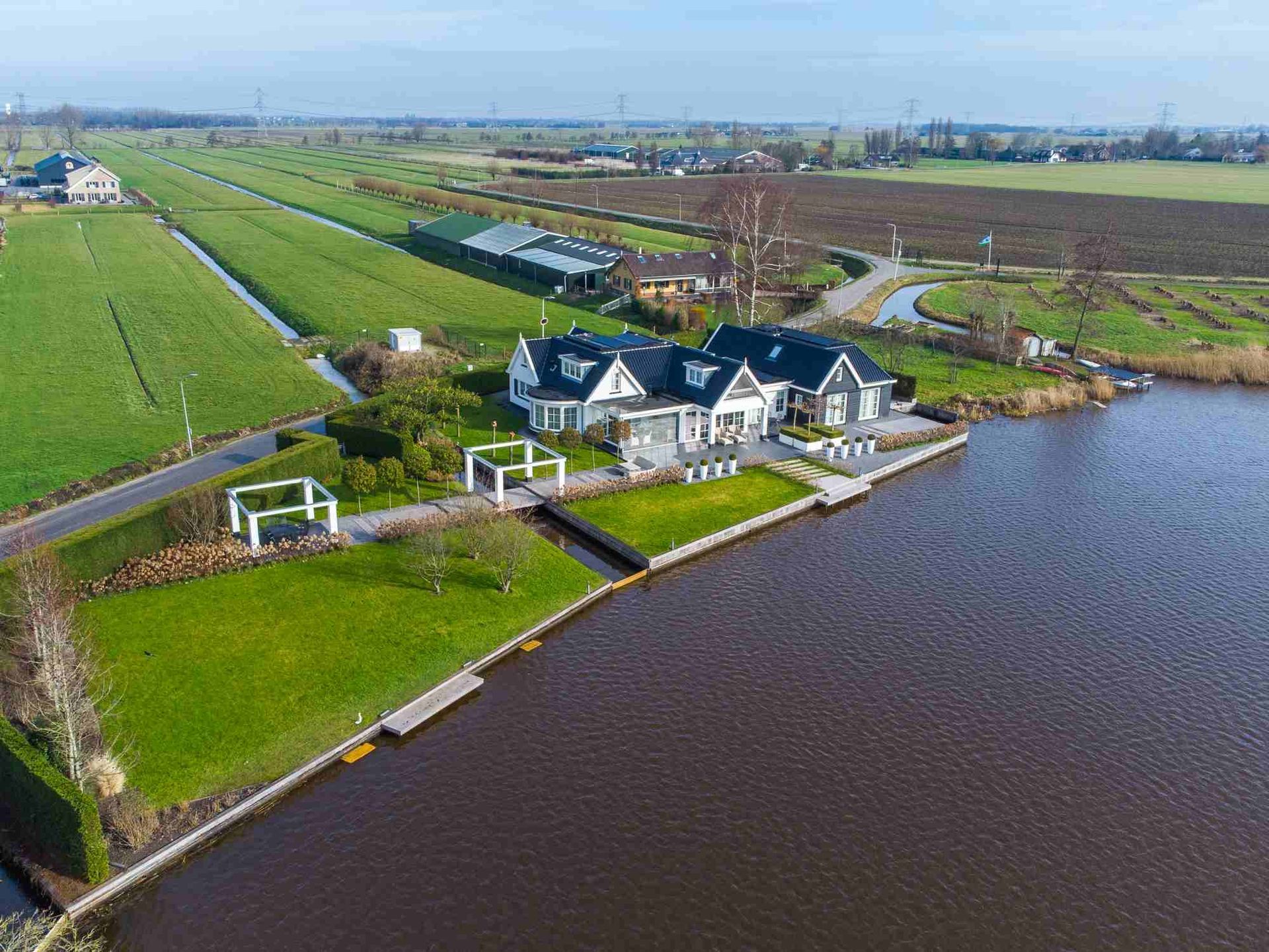 Een luchtfoto van een huis naast een waterpartij, omgeven door velden.