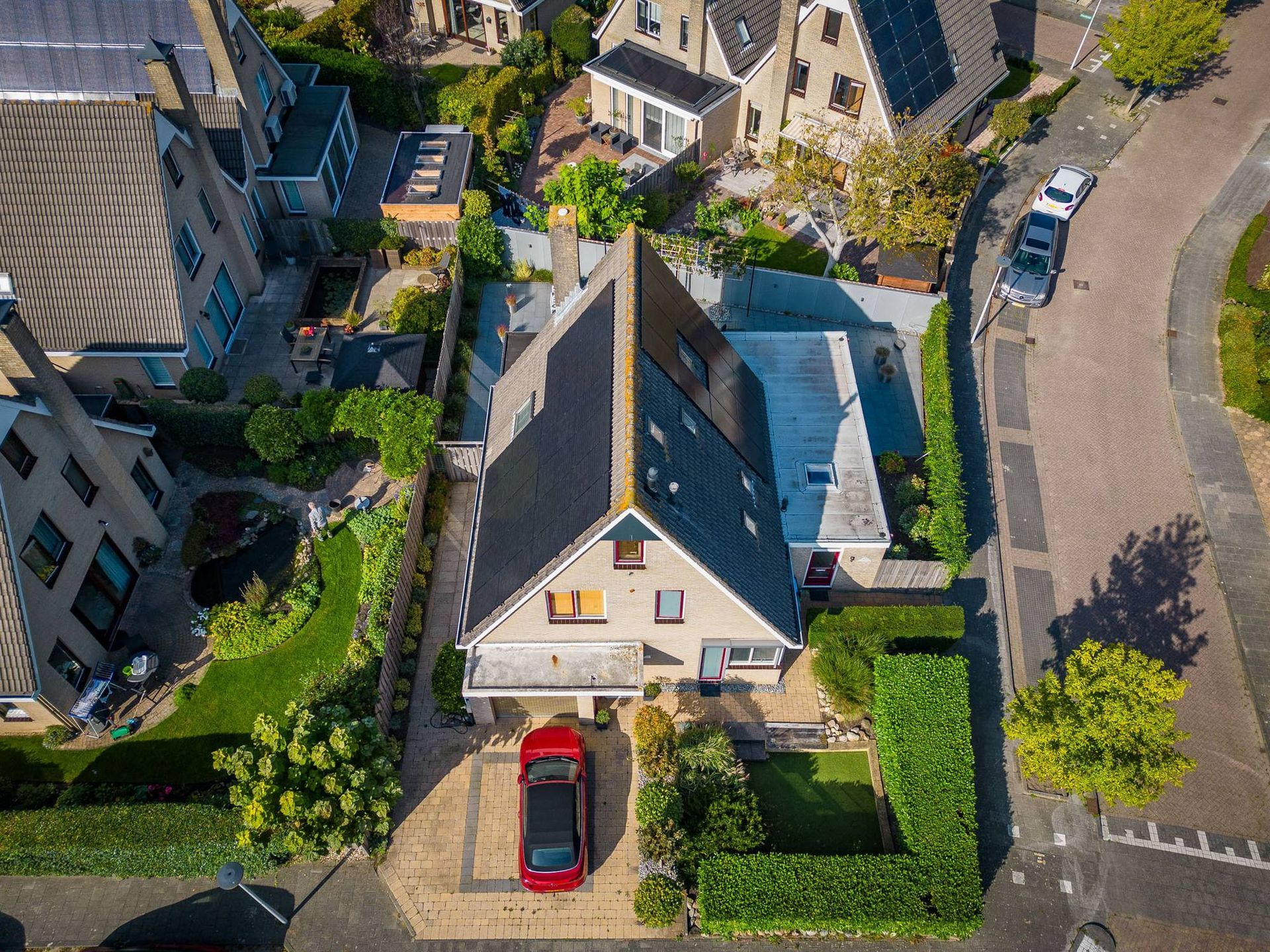 Een luchtfoto van een huis met een rode auto ervoor geparkeerd.