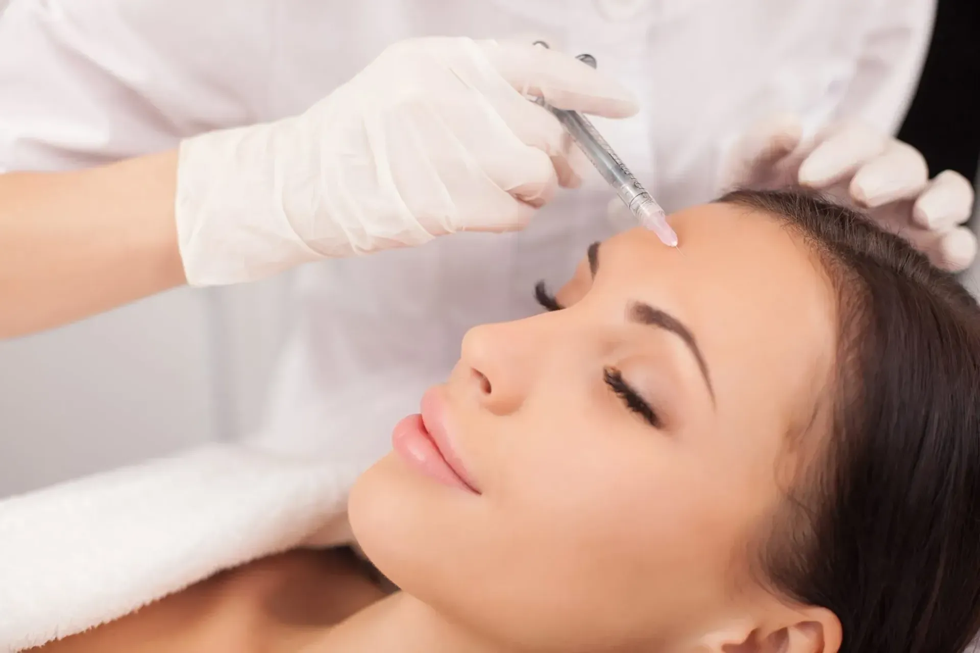 Cosmetician injecting filler into a woman’s forehead during a facial treatment
