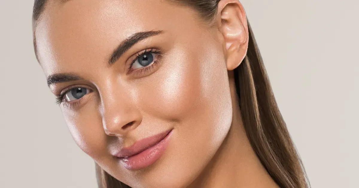 Close-up of a smiling woman with glowing skin against a light background