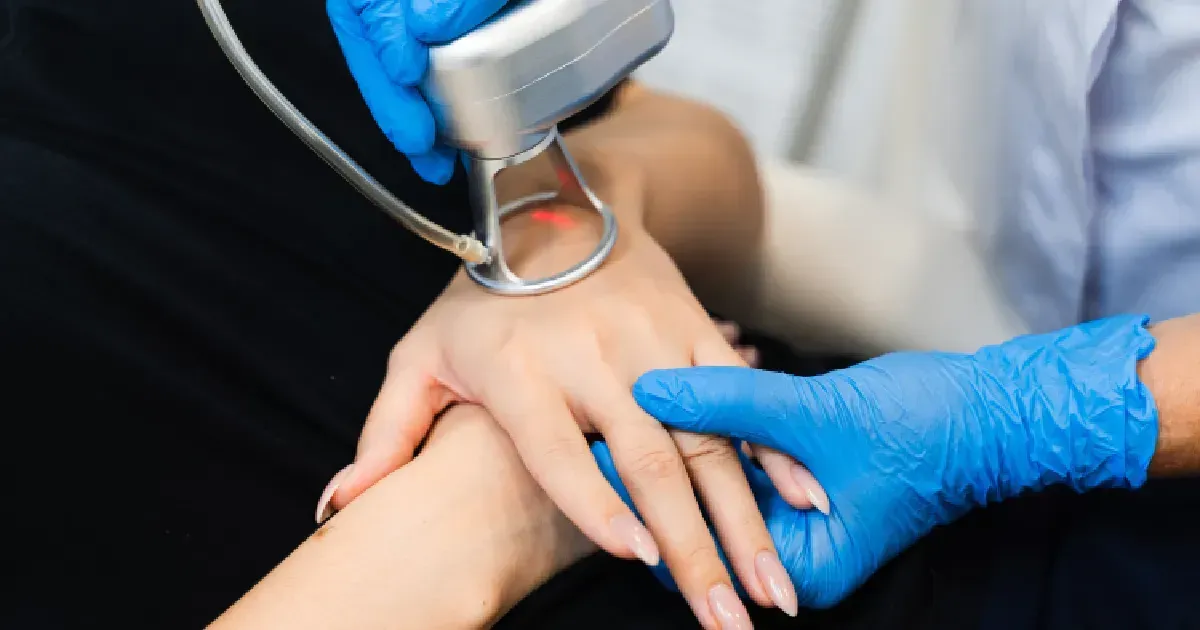Gloved hands applying a handheld medical device to a patient’s wrist during a procedure