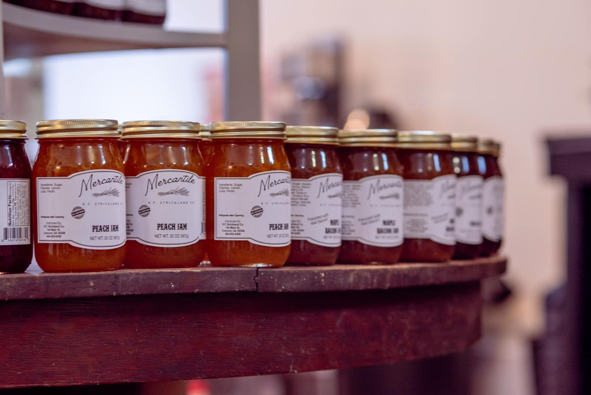 A row of jars of jam are lined up on a wooden shelf.