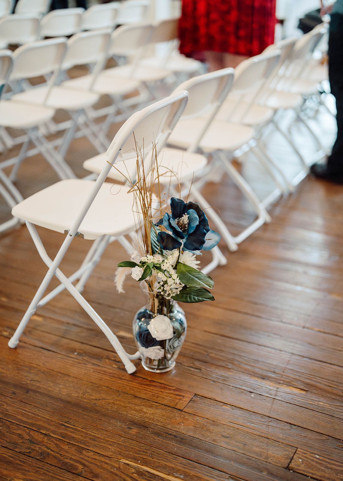 A vase of flowers is sitting on the floor next to a row of folding chairs.