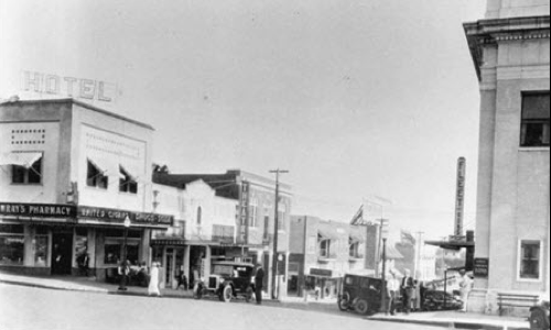 A black and white photo of a city street with a hotel in the background
