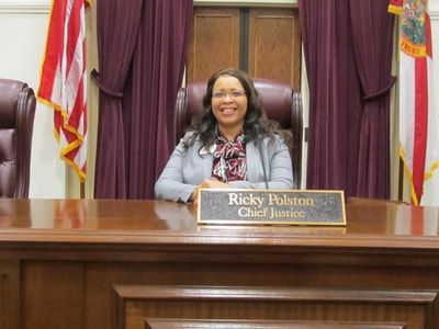 A woman is sitting at a desk with a name plate that says ricky fulton chief justice.