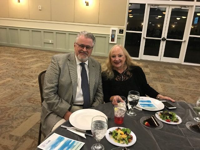 A man and a woman are sitting at a table with plates of food and wine glasses.