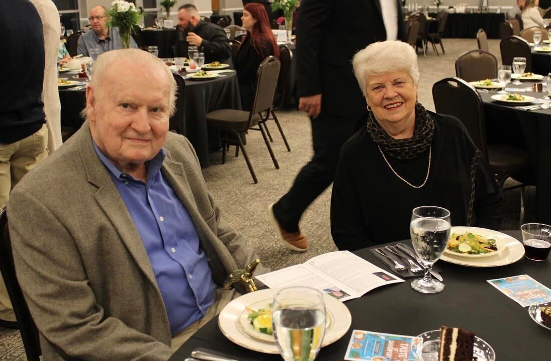 A man and a woman are sitting at a table with plates of food and glasses of water.