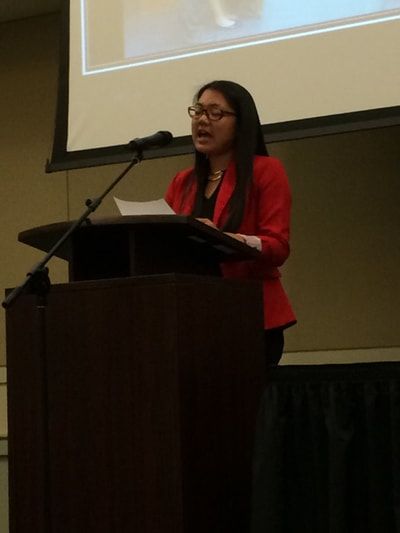 A woman in a red jacket is giving a speech at a podium