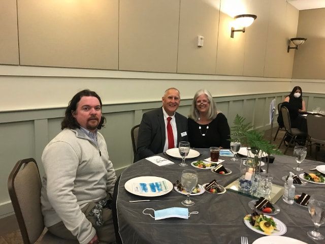 Three people are sitting at a table with plates of food and wine glasses.