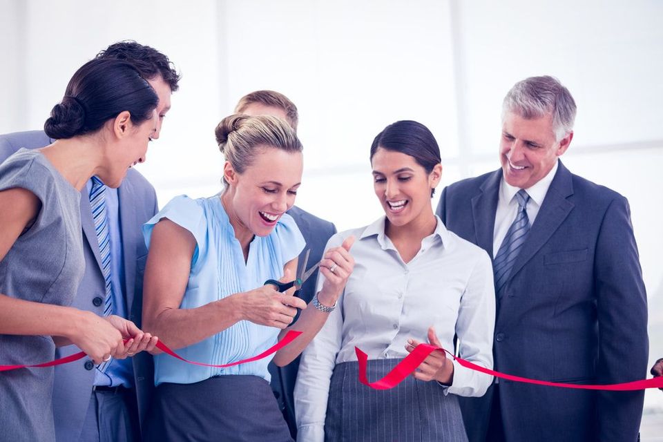 A group of business people are cutting a red ribbon.