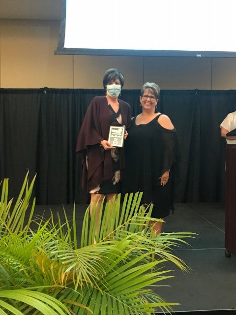 Two women wearing masks are standing on a stage holding a certificate.