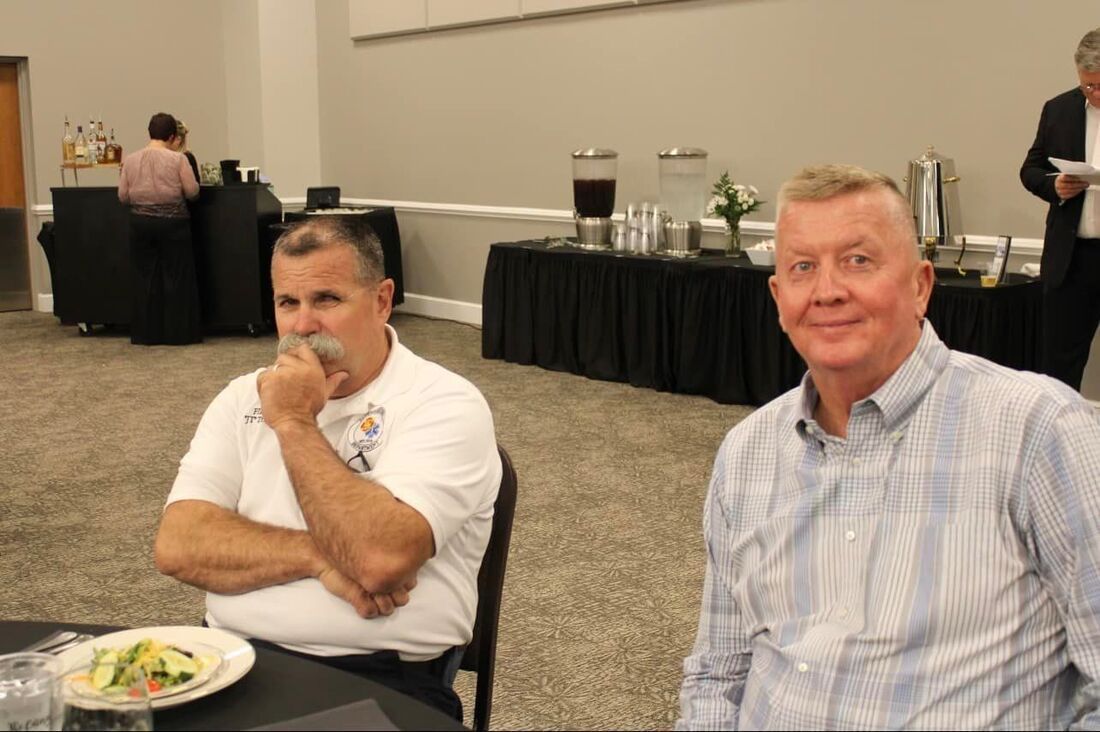 Two men are sitting at a table with plates of food.