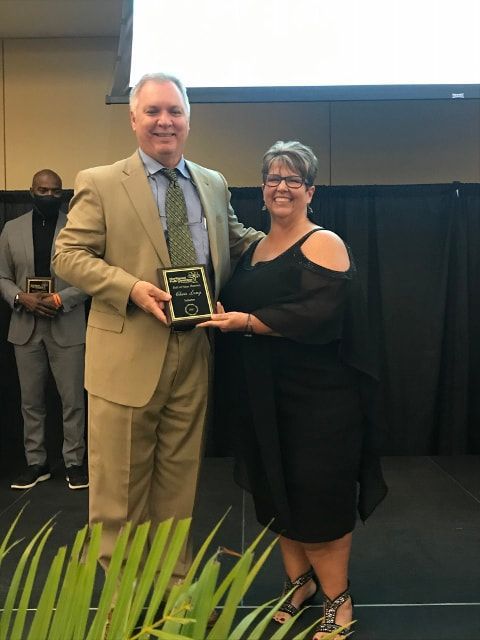 A man in a suit is holding a plaque next to a woman in a black dress.