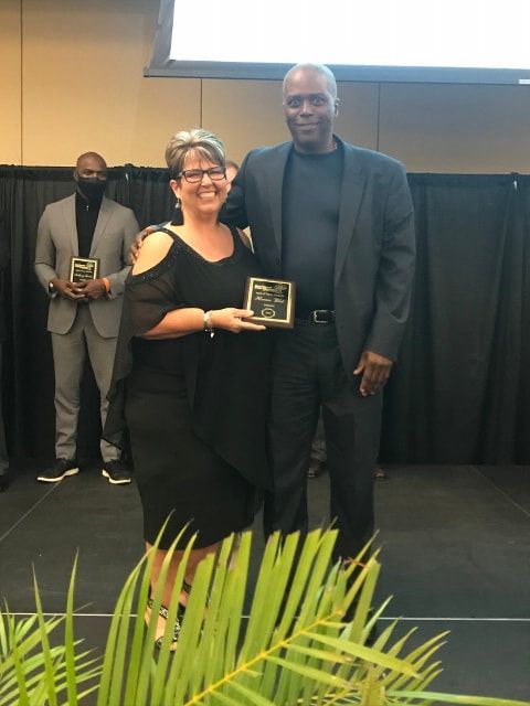A man and a woman are standing on a stage holding awards.