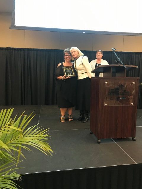 Two women are standing next to each other on a stage holding a plaque.