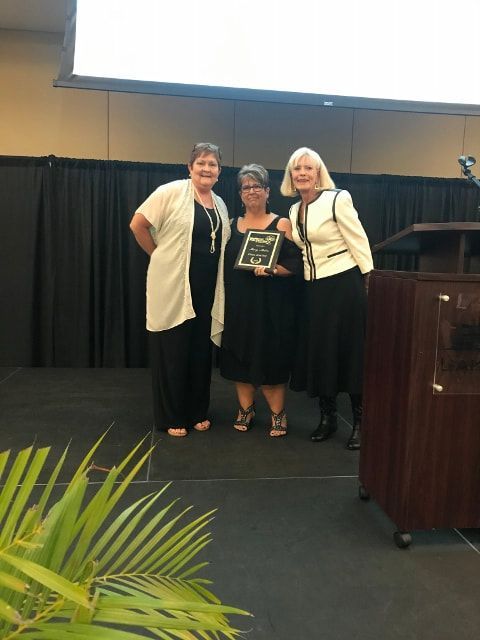 Three women are standing on a stage holding an award