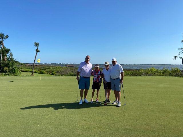 A group of people standing on a golf course holding golf clubs