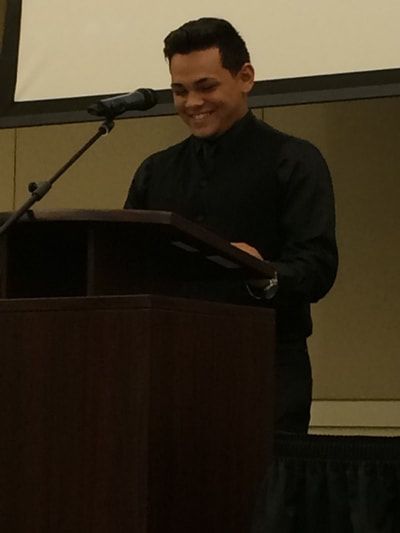 A man in a black shirt stands at a podium with a microphone