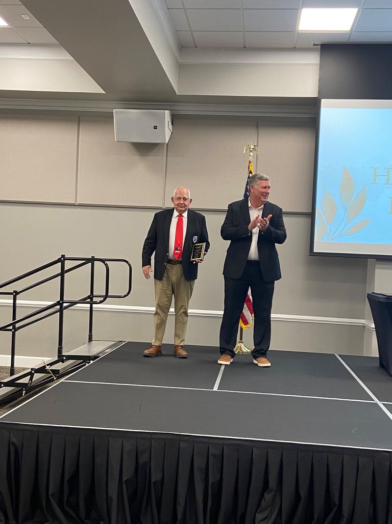 Two men are standing on a stage in front of a projector screen.