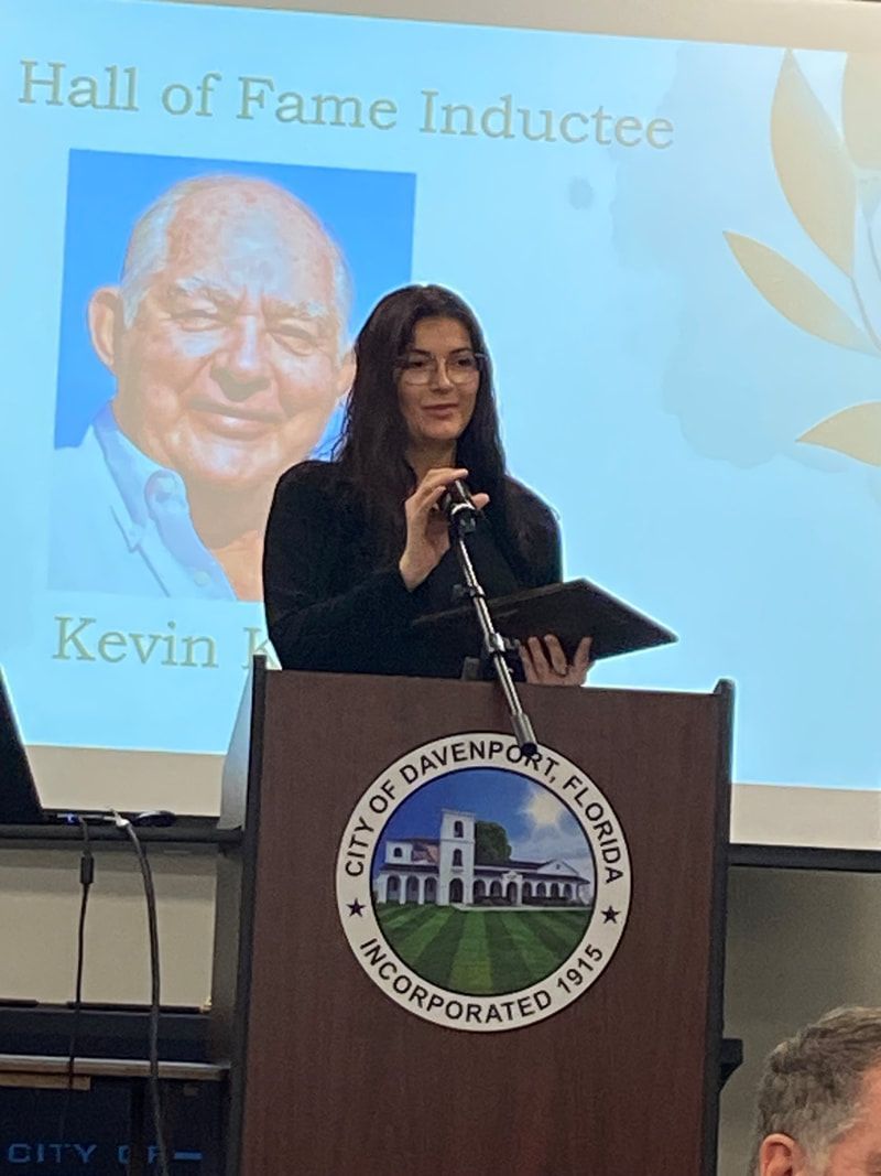A woman is giving a speech at a podium in front of a screen that says hall of fame inductee kevin