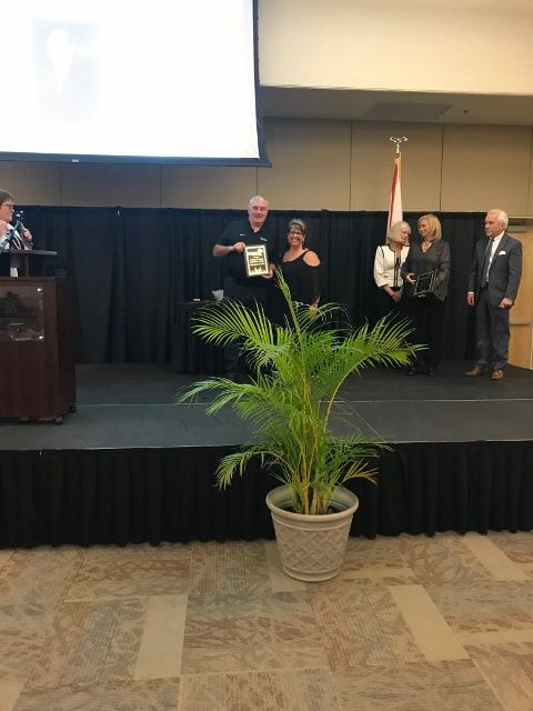A group of people standing on a stage with a plant in front of them.