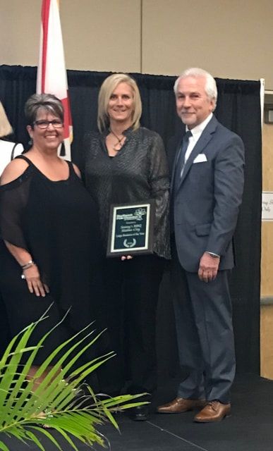 Two women and a man standing next to each other with a woman holding an award