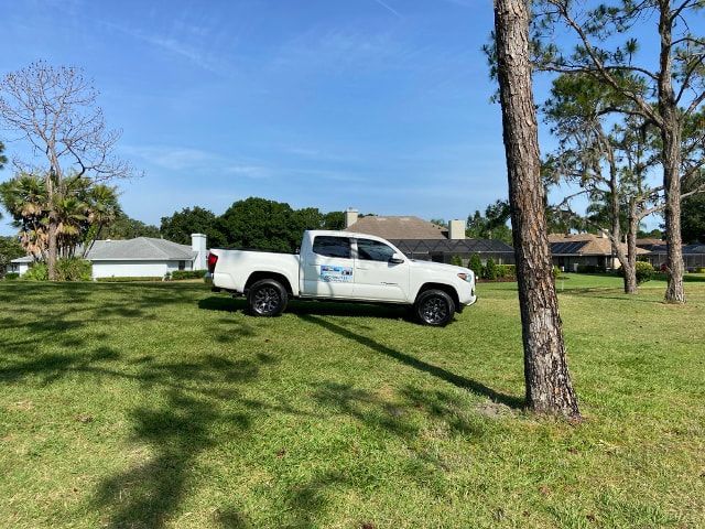 A white truck is parked in a grassy field next to a tree.