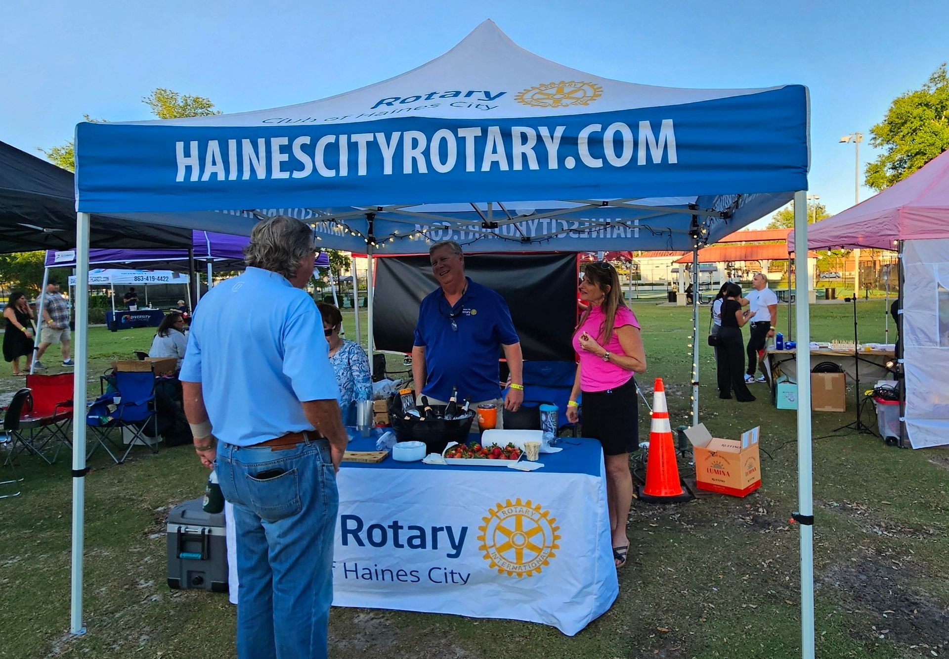 A group of people standing around a table under a canopy that says hainescityrotary.com