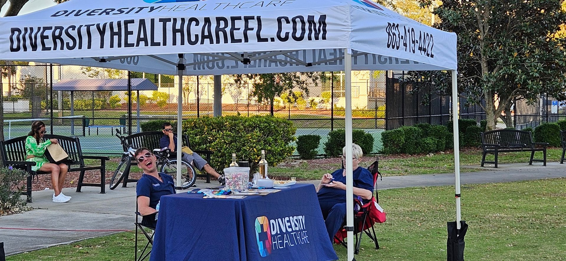 A group of people are sitting under a tent in a park.