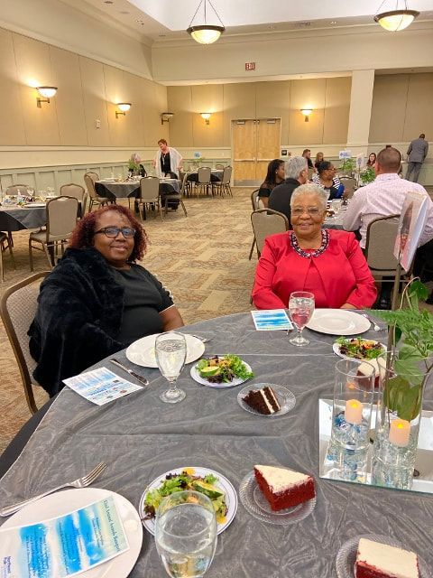 Two women are sitting at a table with plates of food and wine glasses.