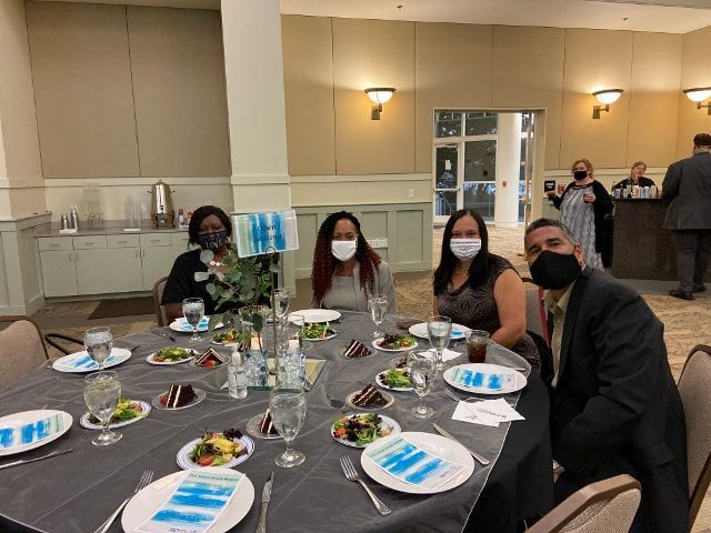 A group of people wearing face masks are sitting at a table with plates of food.