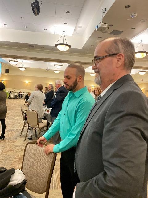 A man in a green shirt is standing next to another man in a suit