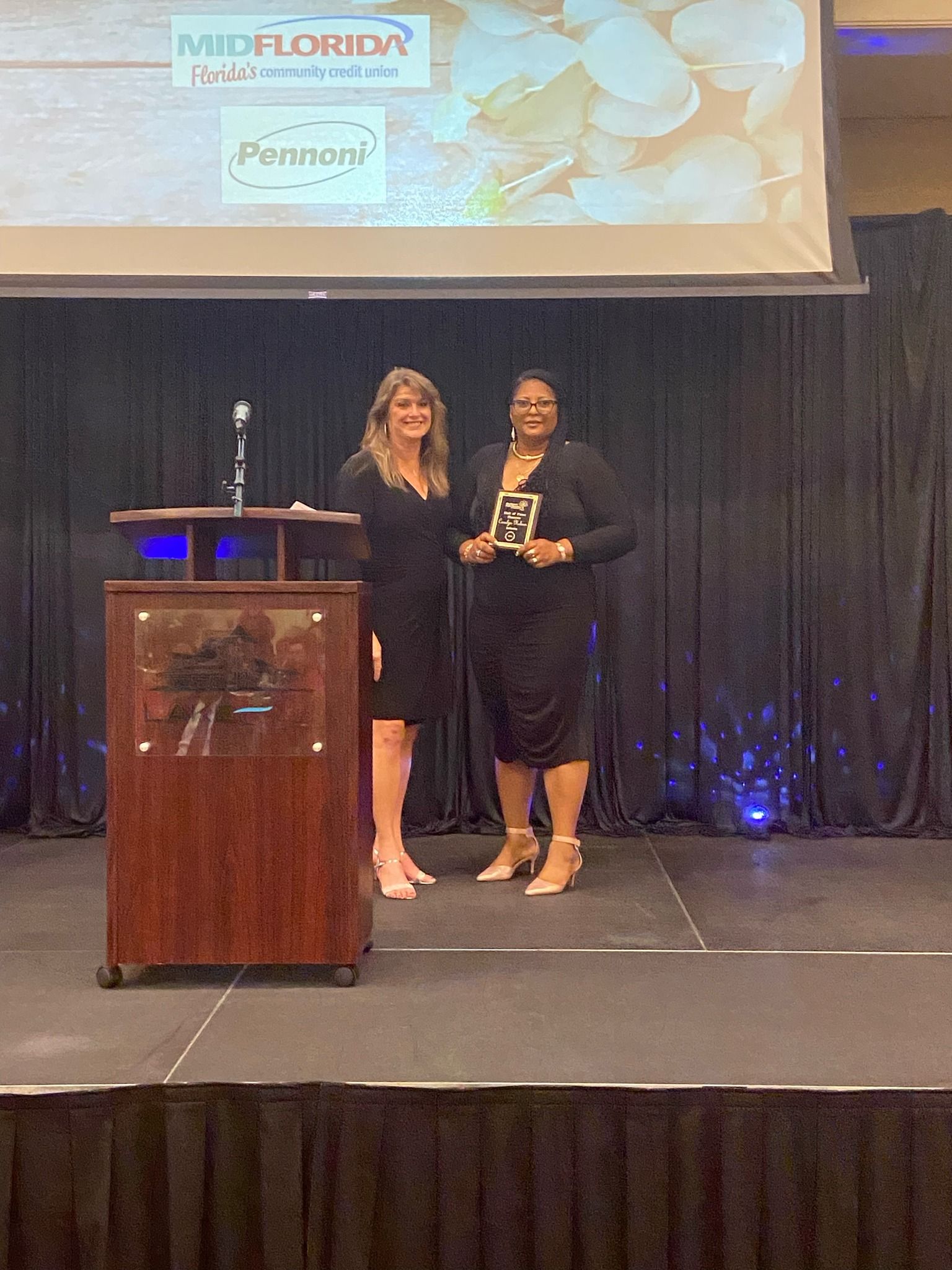 Two women are standing on a stage holding awards.