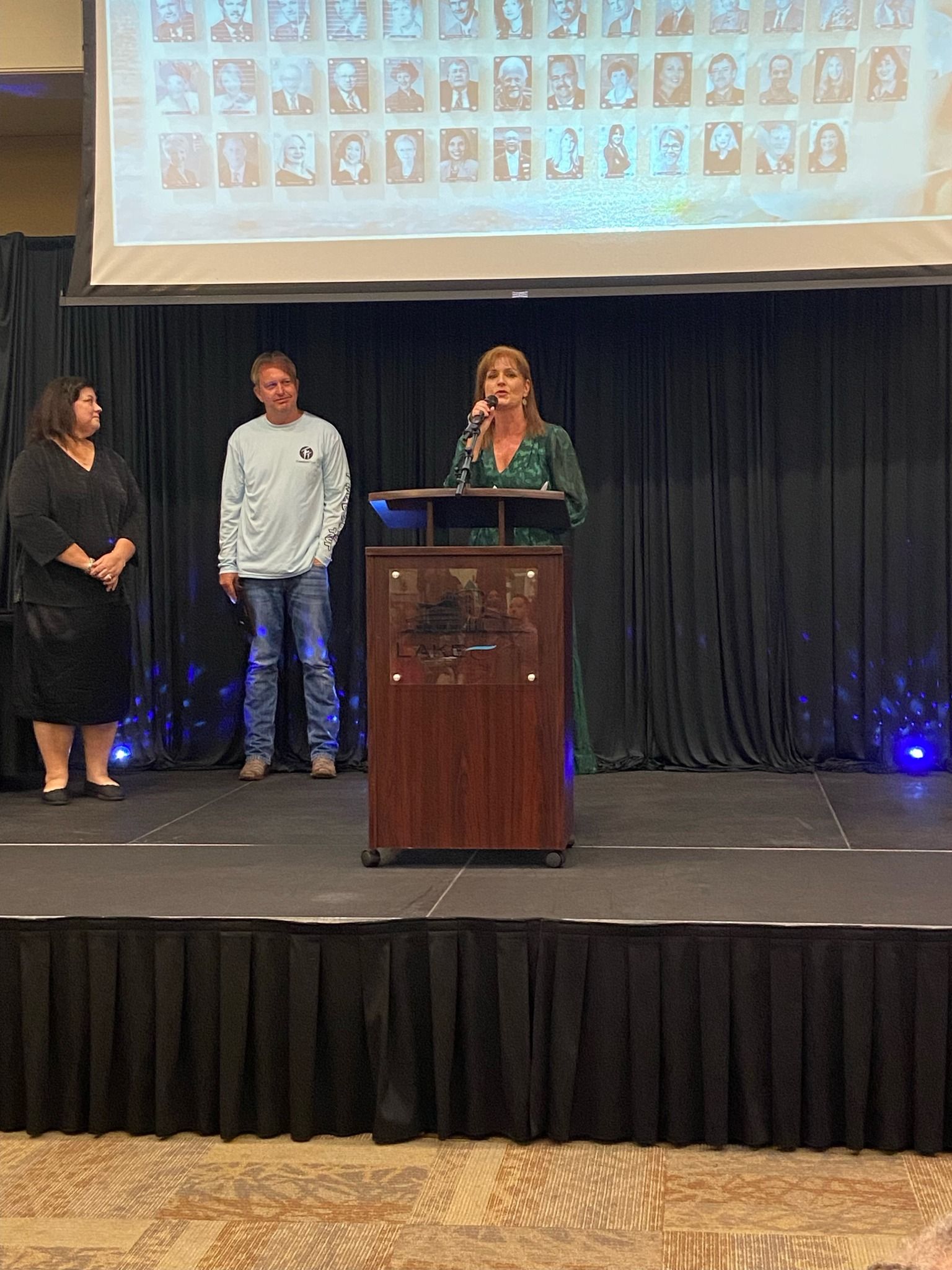 A woman is standing at a podium giving a speech while two people stand behind her.