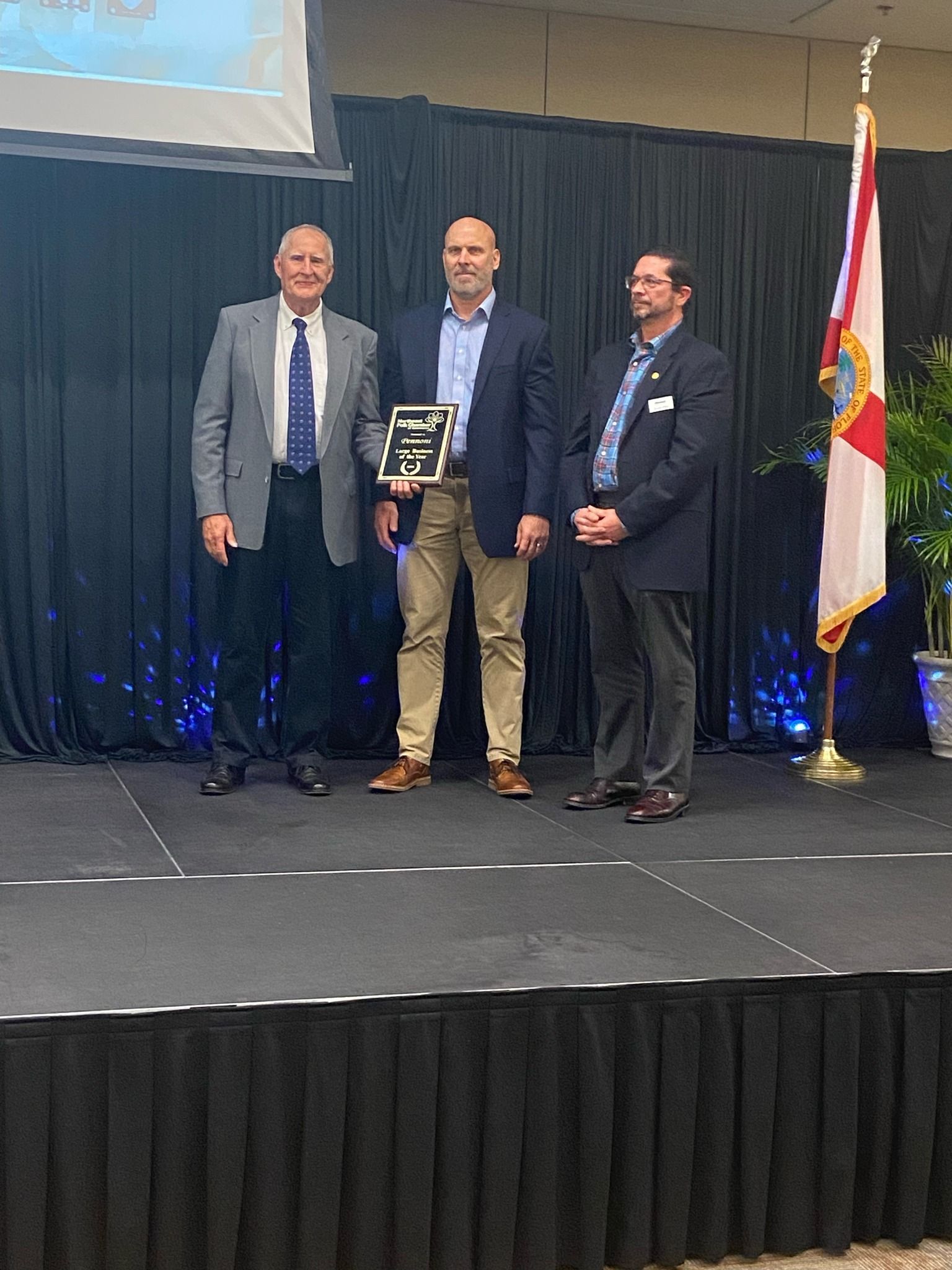 Three men are standing on a stage holding a plaque.