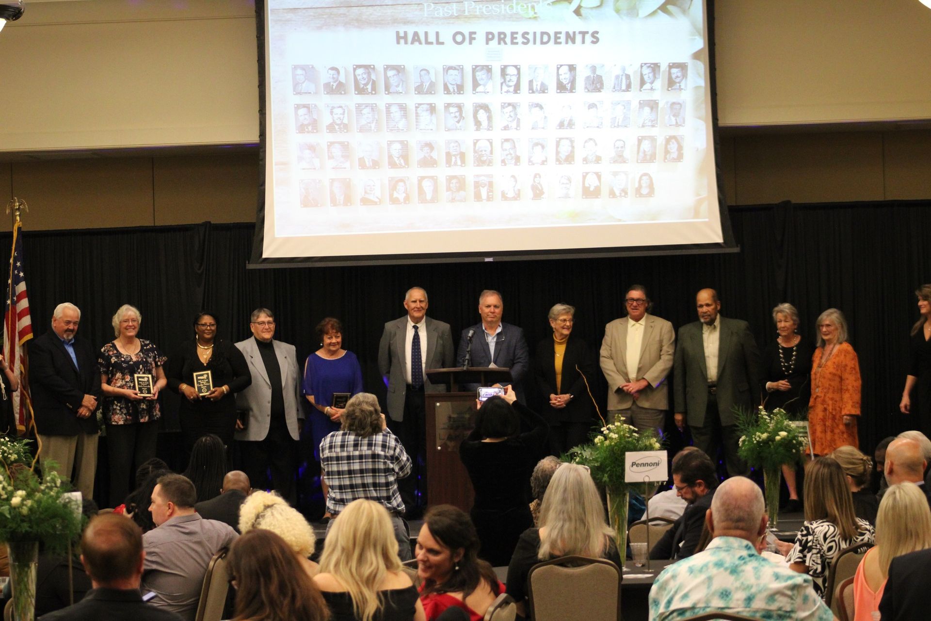 A group of people are standing in front of a screen that says hall of presidents.