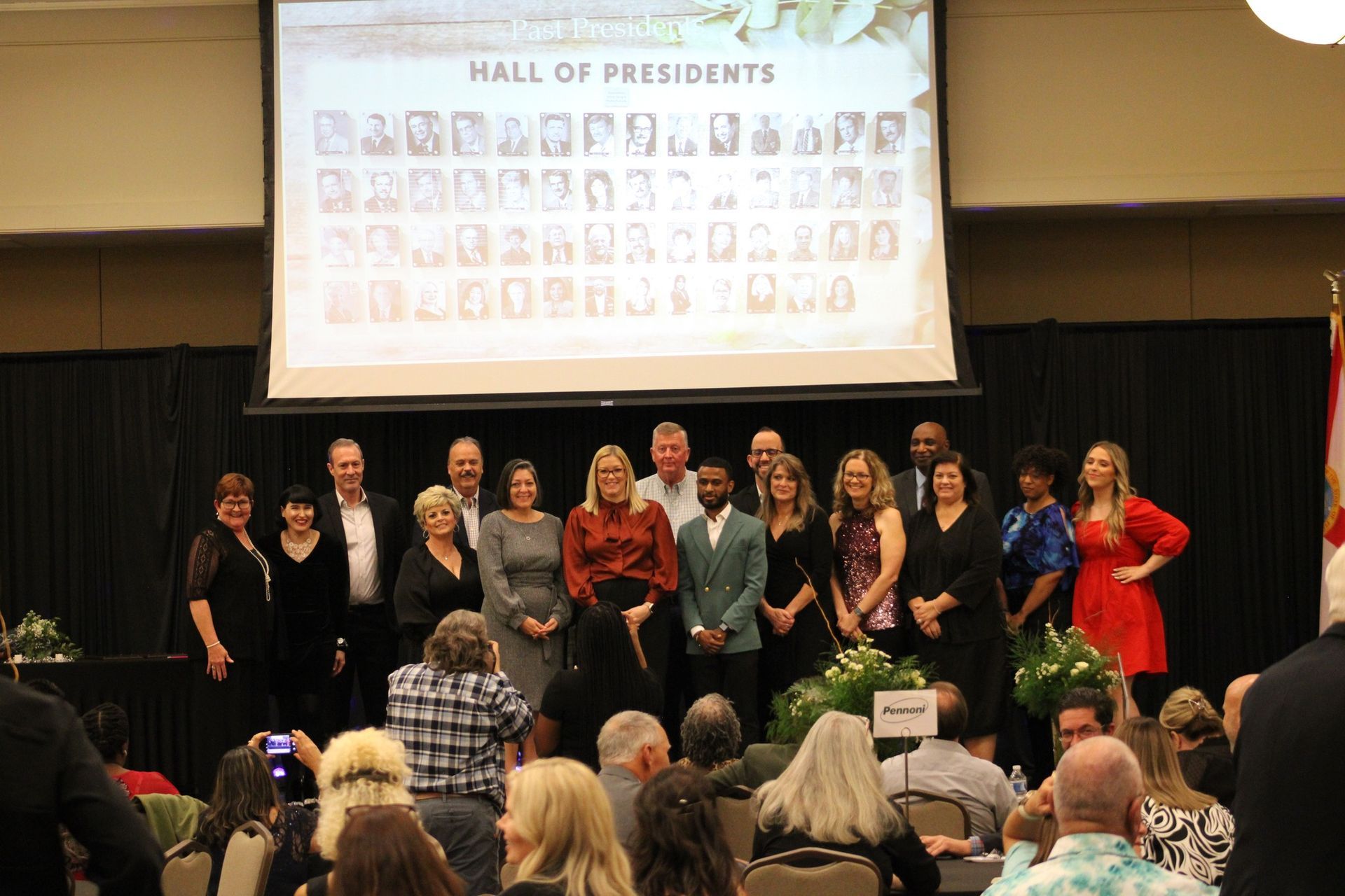 A group of people are standing in front of a screen that says hall of presidents.