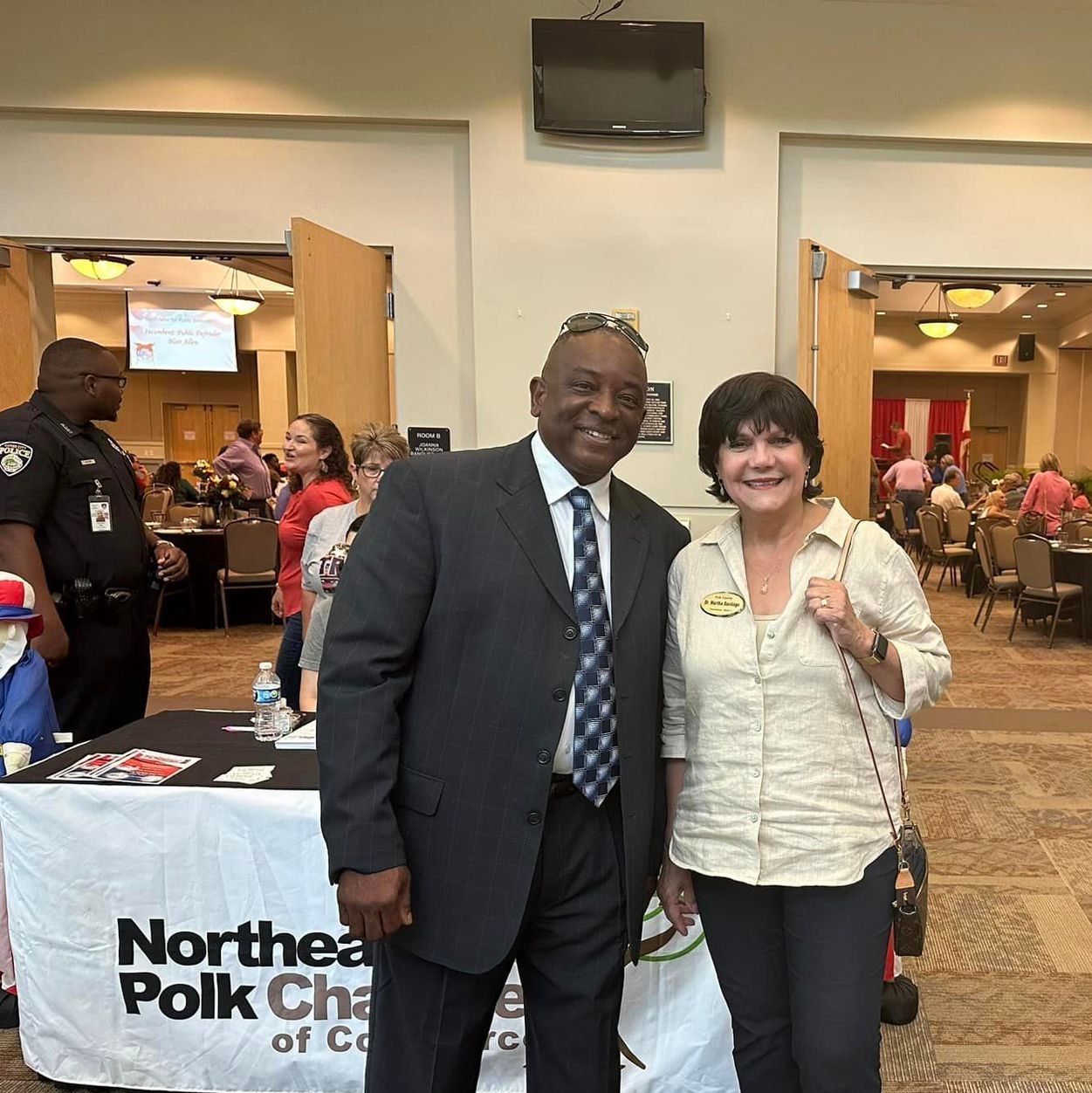 A man and woman are posing for a picture in front of a table that says northea polk chamber of commerce