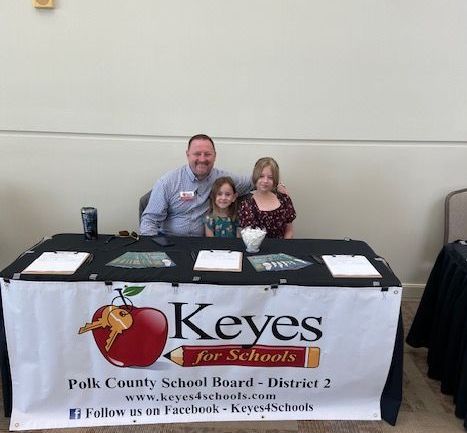 A man and two children are sitting at a table with a sign that says keyes for schools.
