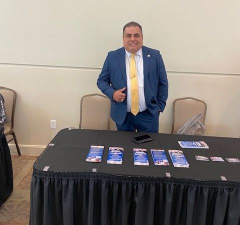 A man in a suit and tie is standing in front of a table.