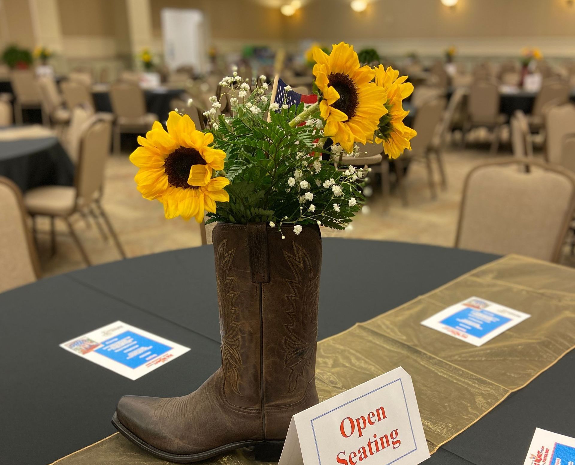 A cowboy boot filled with sunflowers sits on a table next to a sign that says open seating