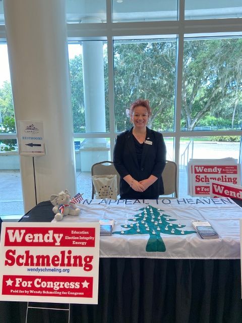 A woman stands behind a table with a sign that says wendy schmeling for congress