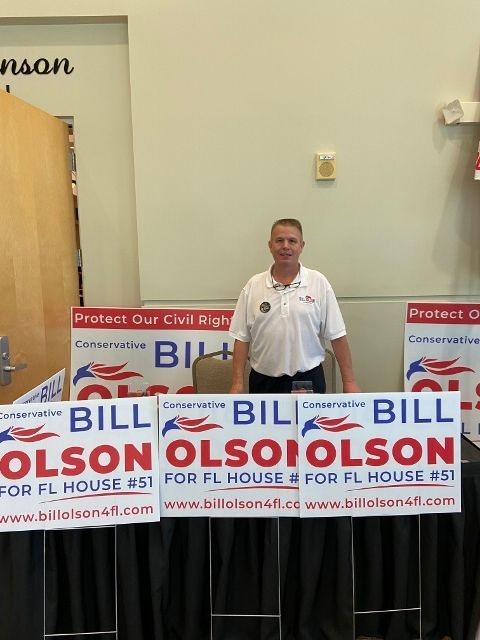 A man stands in front of a table full of bill olson signs