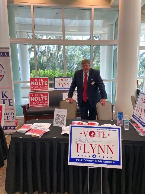 A man stands behind a table with a sign that says vote flynn