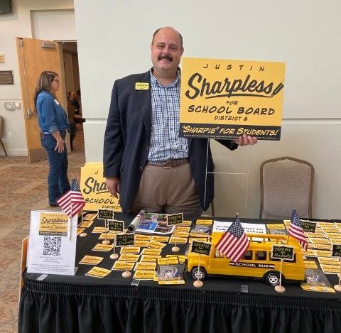 A man is holding a sign that says sharpless for school board
