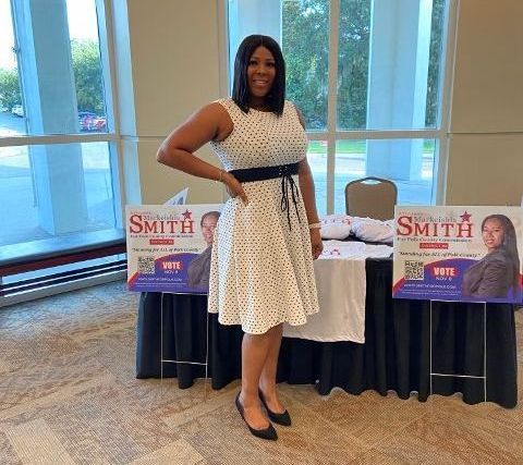 A woman in a white dress is standing in front of a table with signs for smith on it.