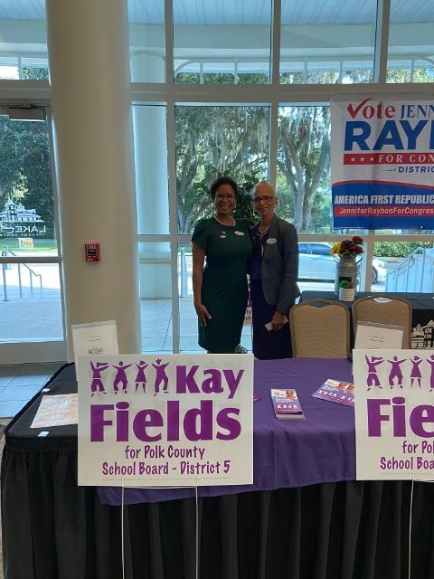 Two women standing in front of a table with signs that say kay fields