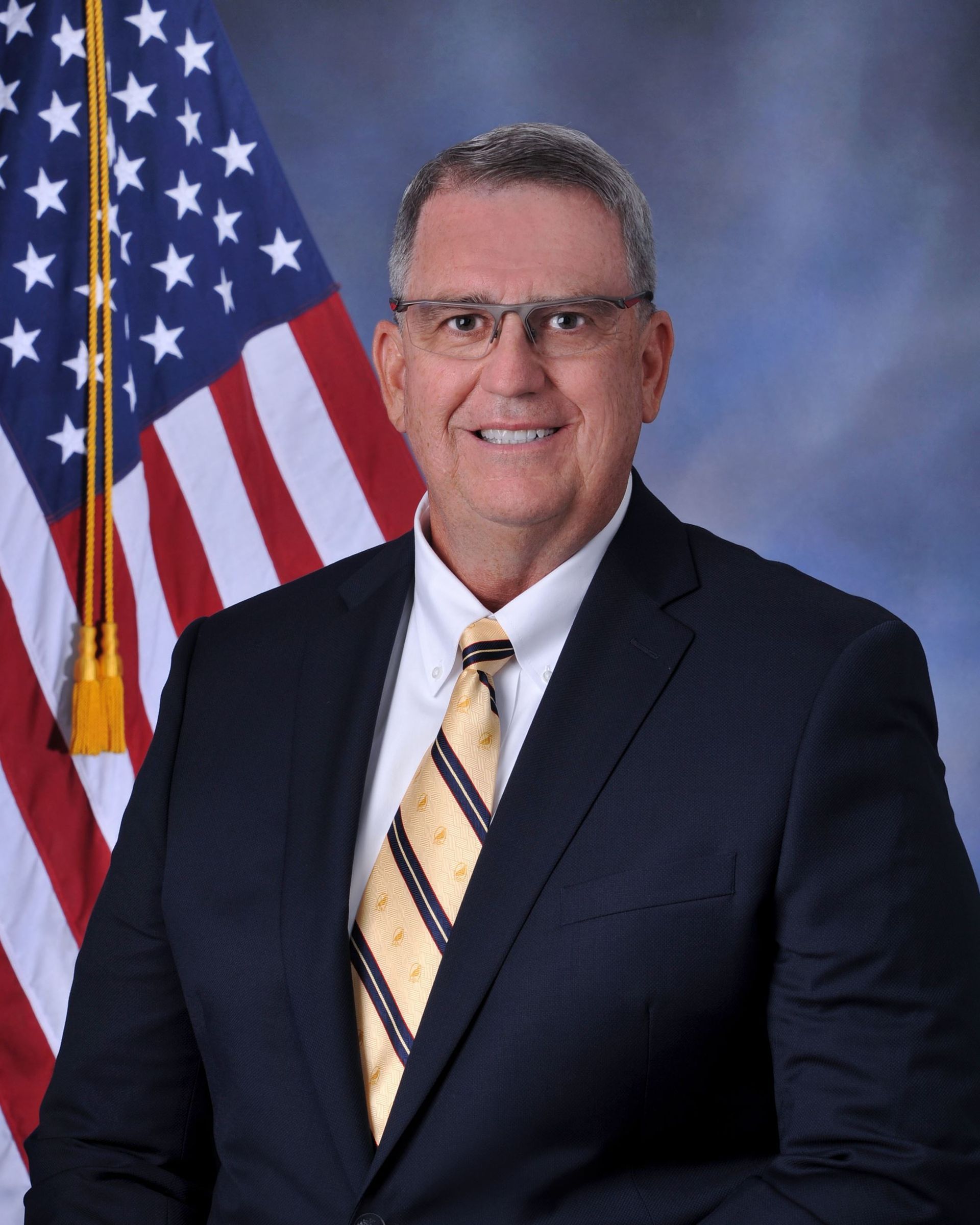 A man in a suit and tie is standing in front of an american flag