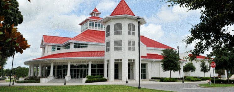 A large white building with a red roof is surrounded by trees.